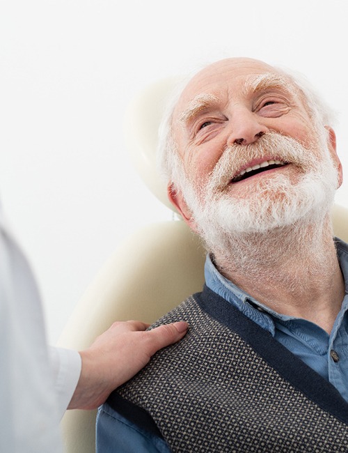 Senior man leaning back in chair and smiling up at dentist