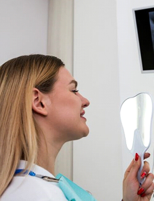 dental patient holding mirror smiling at her reflection